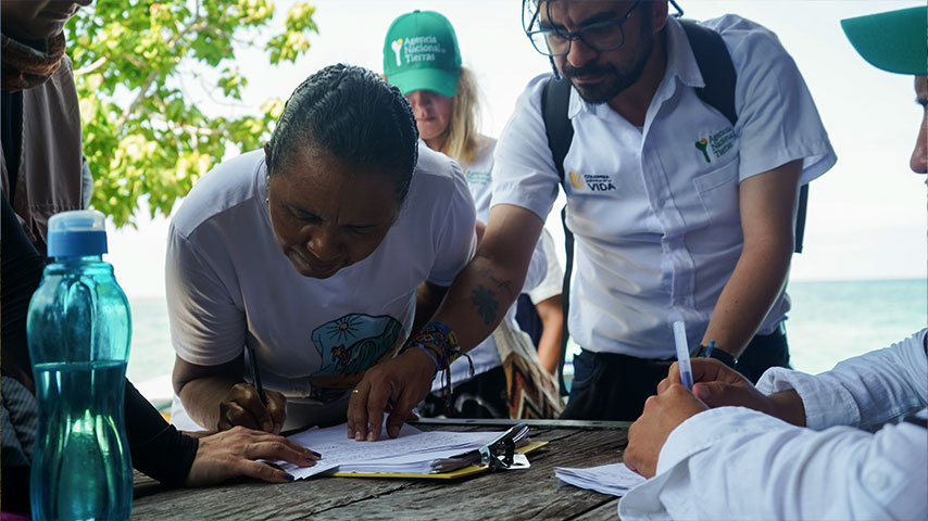Fotografía de una señora firmando un documento acompañada de un funcionario de la ANT.